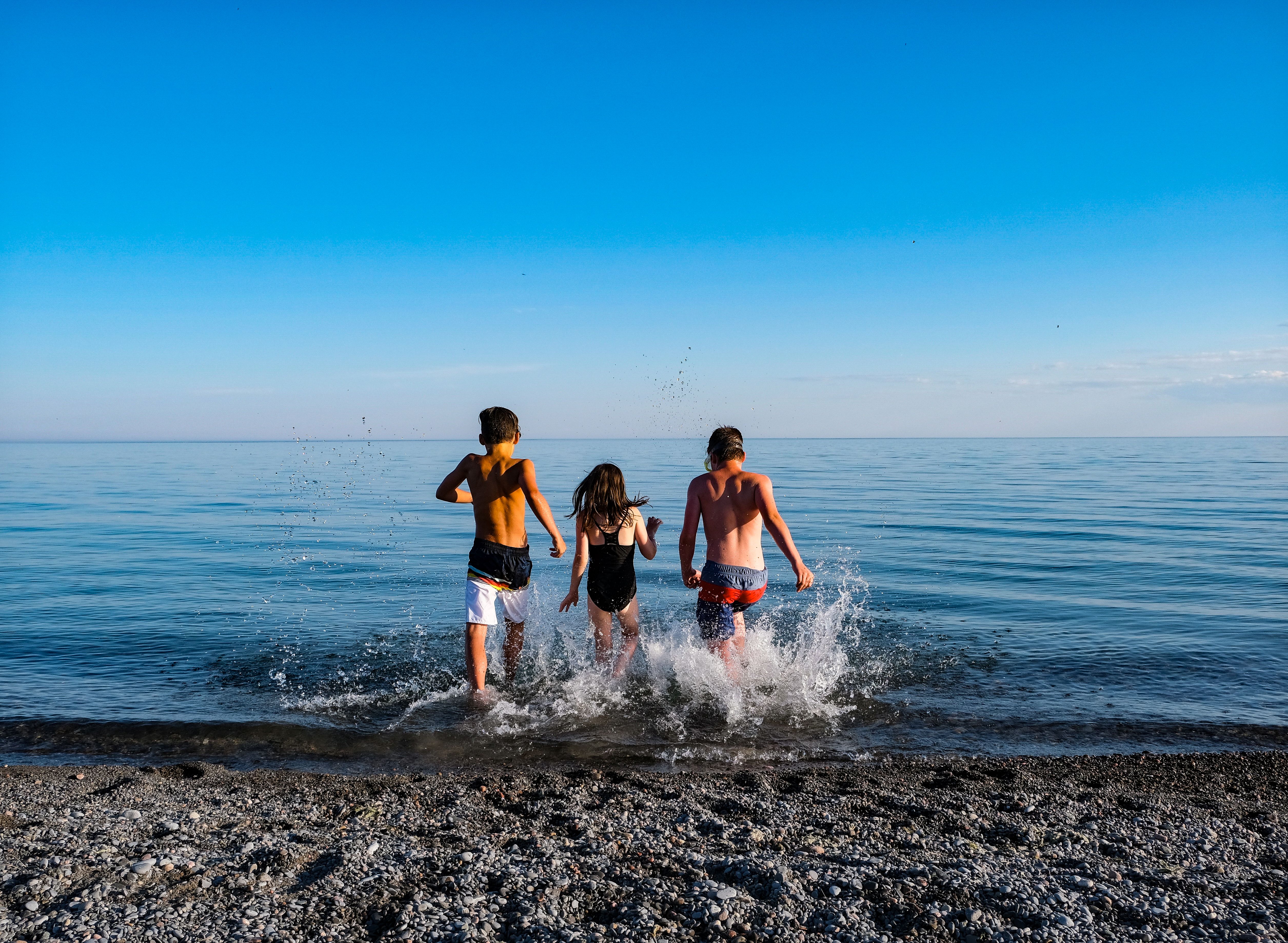 Image of three children running into the water at a beach