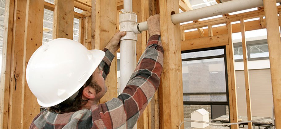 A man fitting a pipe in a newly framed room