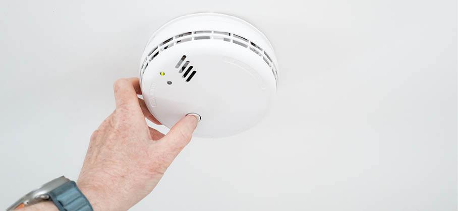 Hand testing a smoke alarm
