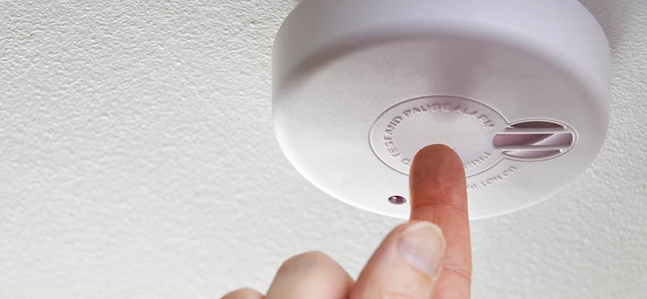 Finger on test button of a smoke alarm