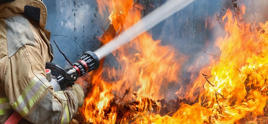 Firefighter with hose spraying water on flames