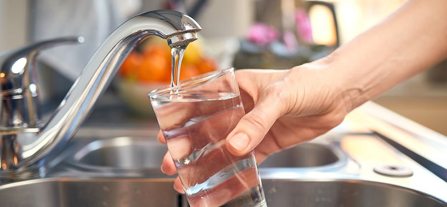 Hand holding a glass under a running tap to fill