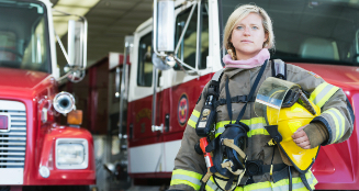 Photo of firefighter standing beside a fire truck.