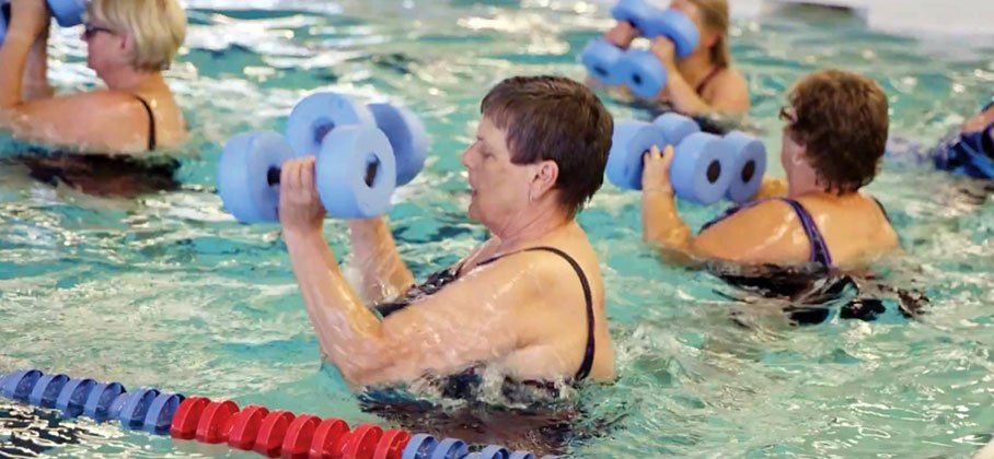 women in an indoor pool lift weights