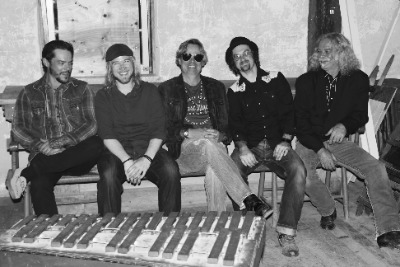 A black and white photo of five band members sitting on a couch