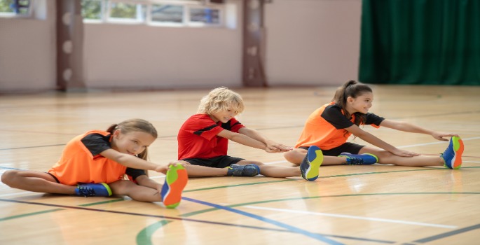 children stretching sitting on a gym floor