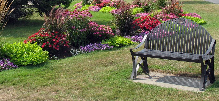 metal park bench on a lawn among flower gardens in full bloom