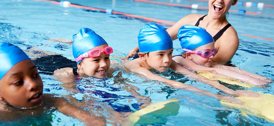 four children in an indoor pool using a flutter board to learn to swim